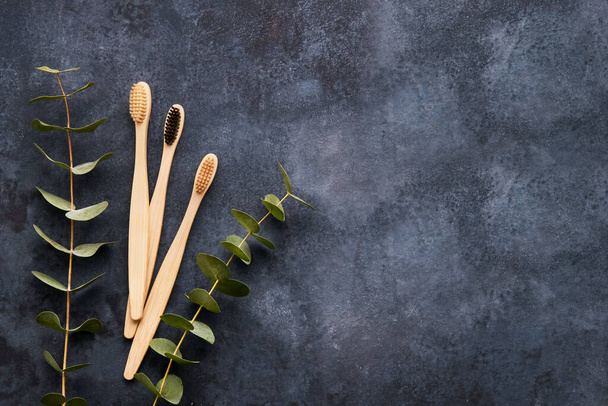 Flat lay composition with eco-friendly bamboo toothbrushes and eucaliptus branch on dark grey background. Zero waste concept. Top view, copy space - Photo, Image