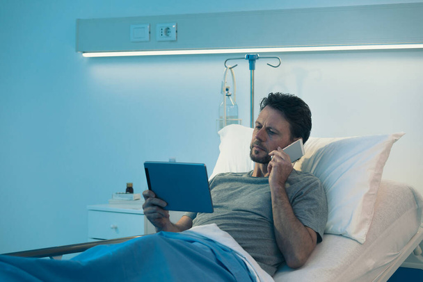 Dorosły bezsenny pacjent leżący w szpitalnym łóżku w nocy, łączy się ze swoim cyfrowym stołem - Zdjęcie, obraz