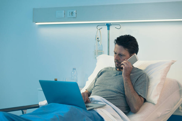 Paciente adulto sem dormir deitado em uma cama de hospital à noite, ele está se conectando com seu lapto - Foto, Imagem