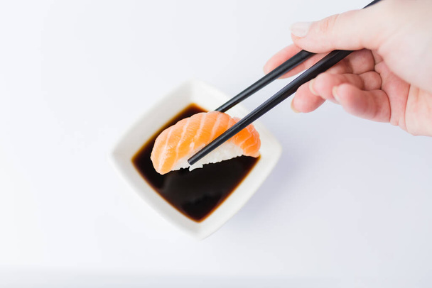 Close up of woman holding chopsticks with salmon sushi roll and bowl with soy sauce on table, japanese traditional healthy meal concept. - Fotó, kép