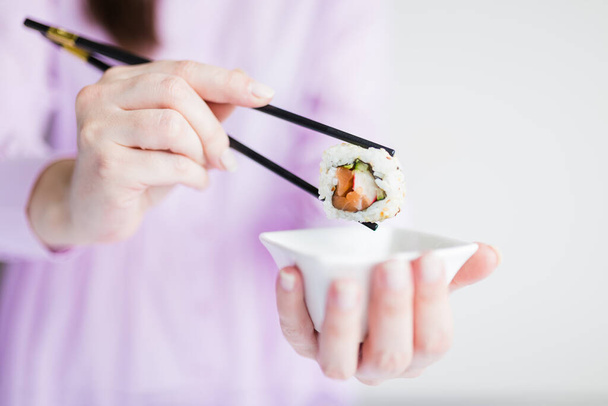 Close up of woman holding bowl with soy sauce and chopsticks with sushi roll, japanese traditional healthy meal concept. - Foto, Bild
