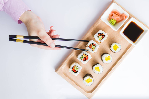 Flat lay of female hand using chopsticks for eating sushi rolls set. - Fotografie, Obrázek