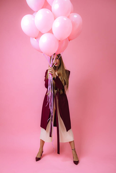 stijlvol jong meisje in bordeaux kleding en roze ballonnen op een roze achtergrond - Foto, afbeelding