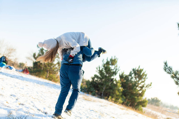 Loving couple play in the winter in the forest. The guy threw the girl on his back and runs with her through the forest. Laugh and have a good time - Φωτογραφία, εικόνα