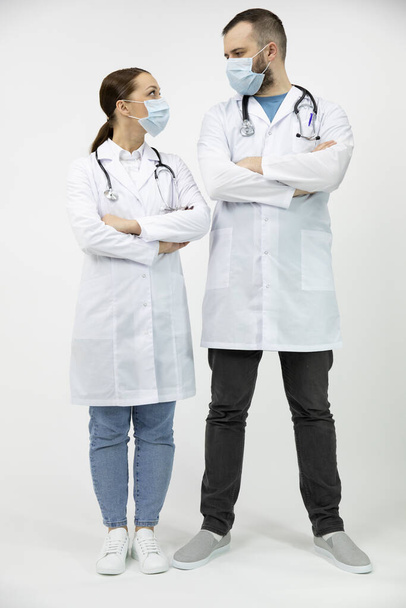 Kaksi lääkäriä lääketieteellisissä naamioissa katsoo toisiaan kädet ristissä. - Valokuva, kuva