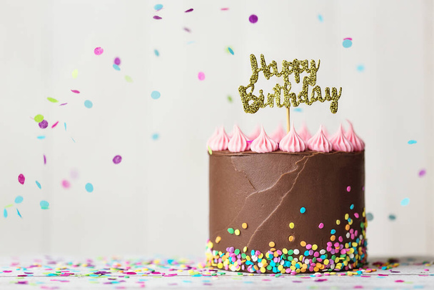 Pastel de cumpleaños de chocolate con pancarta de cumpleaños feliz y confeti cayendo
 - Foto, imagen
