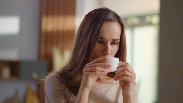 Удовлетворенная женщина пьет чай на кухне. Леди наслаждается чашкой кофе дома
 - Фото, изображение