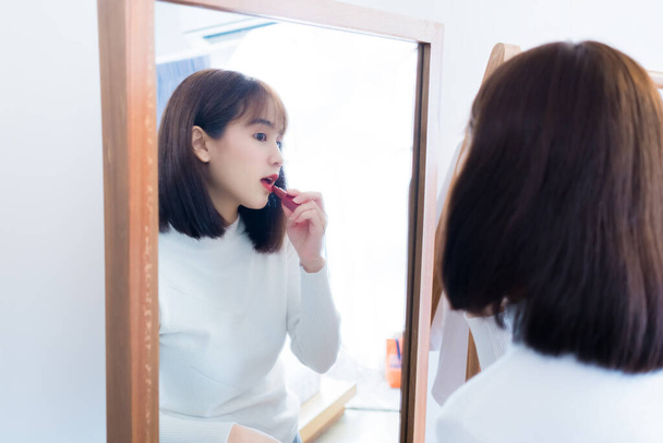 Asian woman choosing make up with cosmatic applying lipstick and smiling happy in front mirror at home people every day look lifestyle. - Foto, imagen