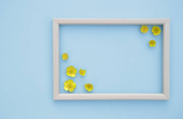 Spring floral background. Frame with fresh yellow flowers on a blue background. The concept of spring. Mother's Day, Women's Day. Flat lay, space for text. View from above. - 写真・画像