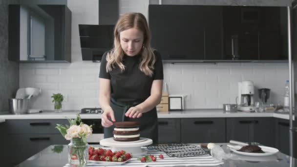 Profesjonalny kucharz gotuje ciasto. Młoda atrakcyjna gospodyni domowa robi słodkie ciasto czekoladowe z białą śmietaną i truskawkami - Materiał filmowy, wideo