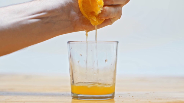 Slow motion of man squeezing orange on wooden table isolated on white - Video