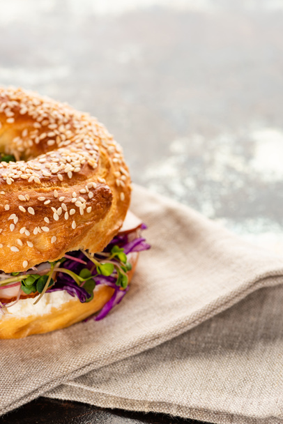 fresh delicious bagel with meat, red onion, cream cheese and sprouts on napkin on textured surface - Fotografie, Obrázek