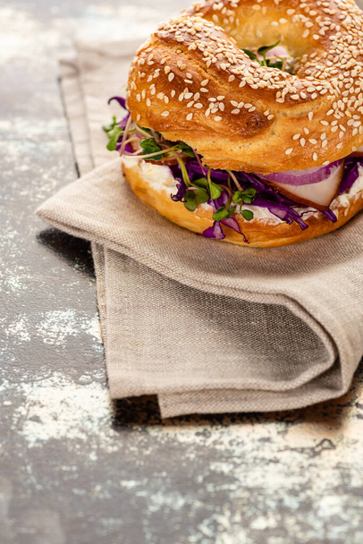 fresh delicious bagel with meat, red onion, cream cheese and sprouts on napkin on textured surface - Φωτογραφία, εικόνα