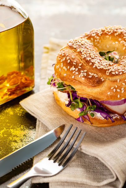 fresh delicious bagel with meat, red onion, cream cheese and sprouts on napkin with cutlery on textured surface - Photo, image