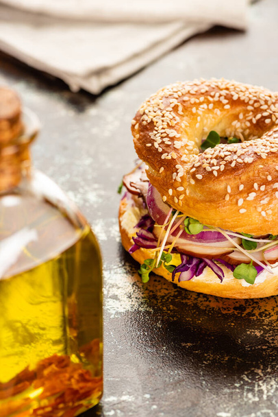 selective focus of oil and fresh delicious bagel with meat, red onion, cream cheese and sprouts on textured surface - Fotoğraf, Görsel