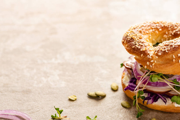 fresh delicious bagel with meat, red onion, cream cheese and sprouts on textured surface - Fotoğraf, Görsel
