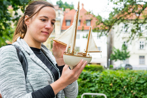 Atrakcyjna kobieta patrząc na model zabawki żagiel łodzi i marzy. - Zdjęcie, obraz