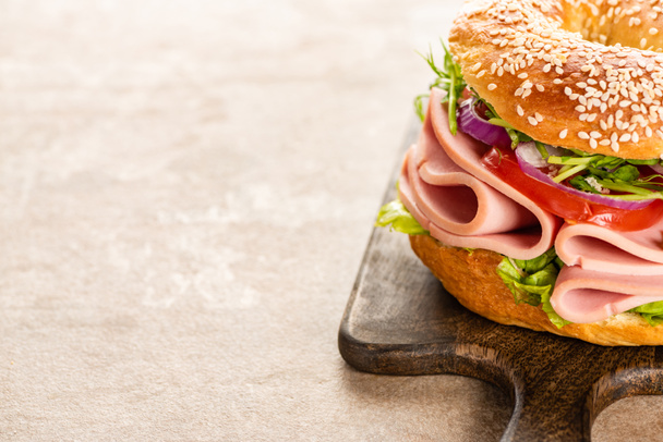 fresh delicious bagel with sausage on wooden cutting board on textured surface - Foto, immagini