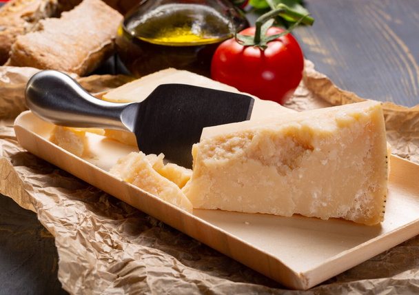 Traditional italian food - aged Italian parmesan hard cheese Parmigiano-Reggiano with cheese knife, tomato, basil, olive oil - 写真・画像