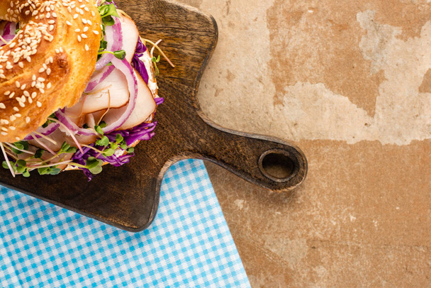 vista superior de bagel delicioso fresco com carne, cebola vermelha, queijo creme e brotos em tábua de corte de madeira e guardanapo azul xadrez
 - Foto, Imagem