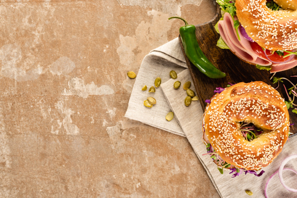 top view of fresh delicious bagels on wooden cutting board on napkin with pumpkin seeds on aged beige surface - Foto, Imagen