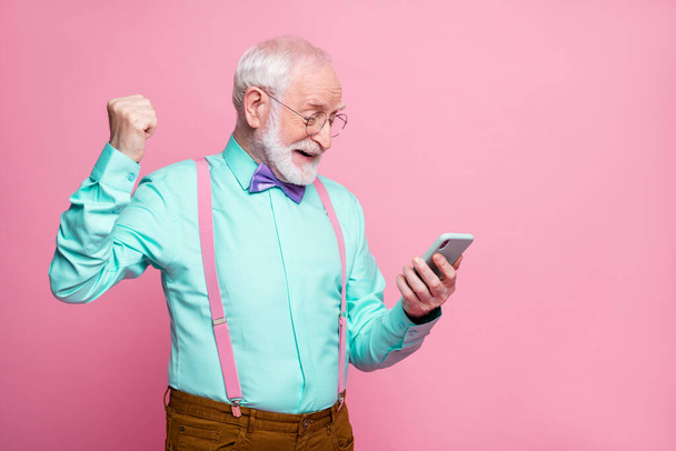 Profile side photo positive retired man use smartphone win social network lottery raise fists scream yes wear turquoise brown pants trousers violet bow tie isolated pastel pink color background - Φωτογραφία, εικόνα