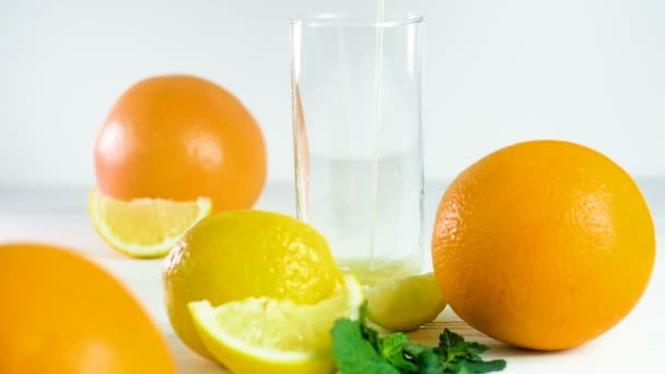  Filmaufnahmen vom Einschenken von Orangensaft in Glas auf weißem Holztisch neben Zitrusfrüchten - Filmmaterial, Video