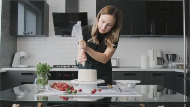 Chef profissional está cozinhando bolo. Jovem dona de casa atraente coloca creme branco em cima do bolo de chocolate
 - Filmagem, Vídeo