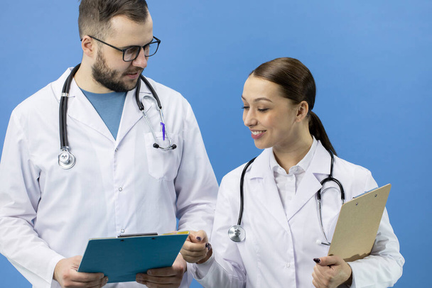 Two positive male and female doctors in white coat analyzing data on clipboard - Photo, Image
