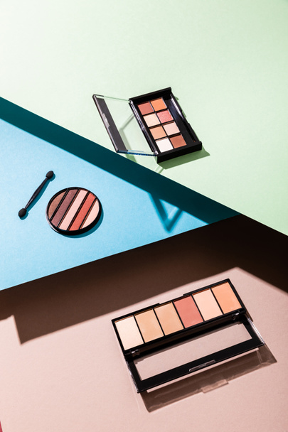 eye shadow palettes and double-sided eyeshadow applicator on blue, green and pink - 写真・画像