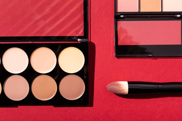 top view of eye shadow and blush palettes near cosmetic brush on crimson  - Φωτογραφία, εικόνα