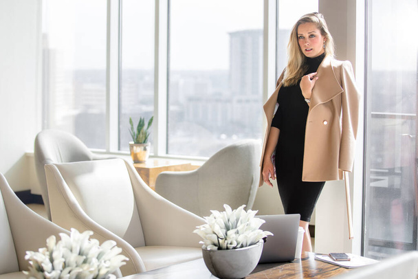 Stylish and elegant, sophisticated professional woman in business attire outfit posing in luxurious workspace lobby with city view with buildings - Foto, afbeelding