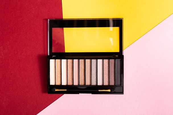 top view of eye shadow palette and double-sided eyeshadow applicator on crimson, pink and yellow - Photo, Image