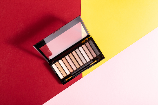 top view of eye shadow palette and double-sided eyeshadow brush on crimson, pink and yellow - Photo, Image
