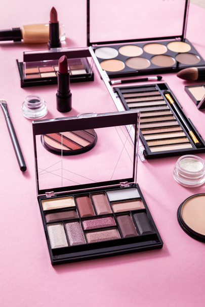 eye shadow and blush palettes near face powder, cosmetic brushes, face foundation and lipsticks on pink  - Photo, image