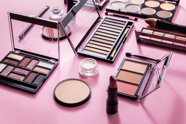 eye shadow and blush palettes near face powder, cosmetic brushes and lipstick on pink  - Photo, Image