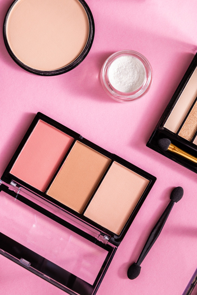 top view of face powder and blush near eye shadow palette on pink - 写真・画像