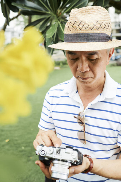 Uomo cinese anziano serio che controlla le foto che ha fatto sulla sua macchina fotografica digitale - Foto, immagini