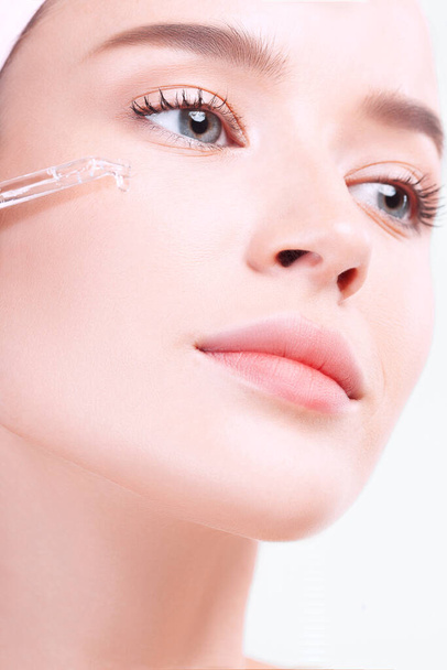 Young beautiful woman with clean perfect skin uses age-sensitive serum in pipette. Skin care and age cosmetics concept - Photo, Image