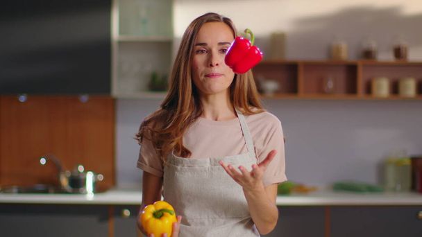 Γυναίκα ρίχνει πιπεριές στην κουζίνα. Νοικοκυρά κοιτάζοντας κάμερα στο σπίτι - Φωτογραφία, εικόνα