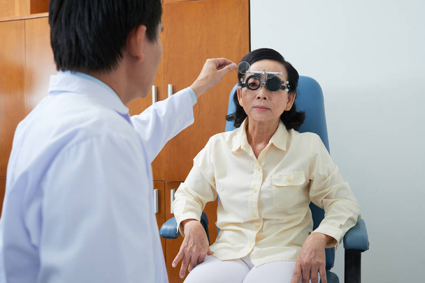 Ophthalmologist examining eyesight of senior patient with special medical device in hospital - 写真・画像