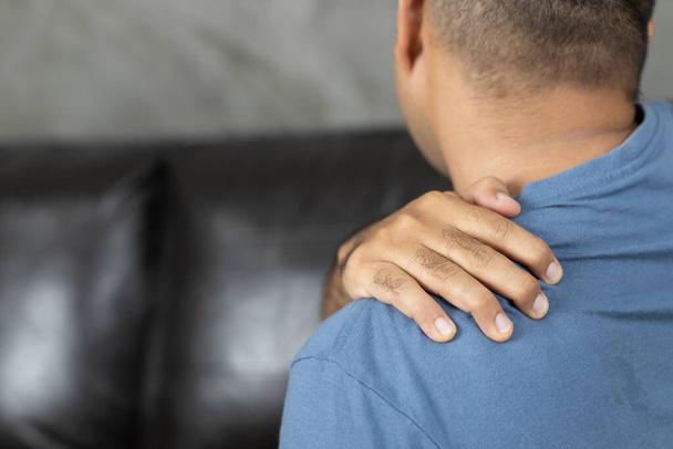 Man heeft nekpijn, schouder pijn zittend op de bank thuis - Foto, afbeelding