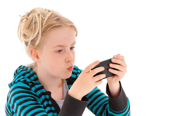 Mooi jong blond meisje starend naar een smartphone. Geïsoleerd op een witte studio achtergrond - Foto, afbeelding