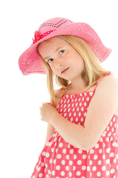 Csinos, fiatal szőke lány rózsaszín sapkában és pöttyös ruhában. Elszigetelt fehér stúdió háttér - Fotó, kép
