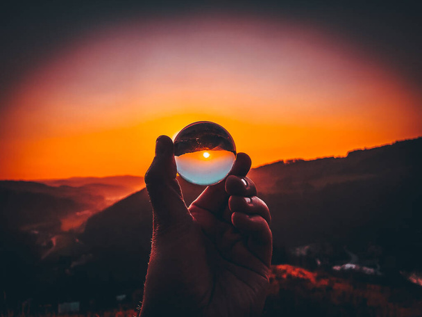 Robienie zdjęć zachodu słońca przez małą szklaną kulkę trzymającą w ręku - Zdjęcie, obraz