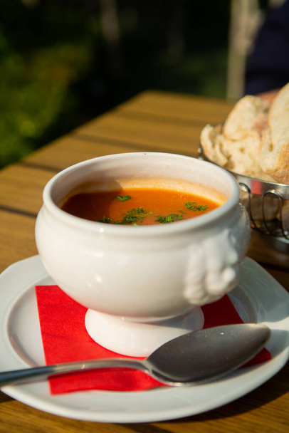 Fresh made vegetables cream soup served in white bowl with bread on outdoor terrace in sunlight - Photo, Image