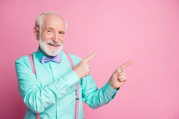 Фото прохладный стильный взгляд пожилой человек парень, указывая пальцы пустое пространство предлагают черную пятницу низкие цены носить подтяжки мяты рубашки фиолетовый галстук бабочка изолированные пастельно-розовый цвет фона
 - Фото, изображение