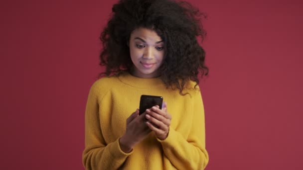 Young african surprised emotional pleased woman isolated over dark red burgundy background showing display of mobile phone - Filmmaterial, Video