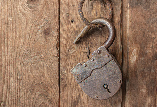 Μια παλιά, σκουριασμένη κλειδαριά κρέμεται ανοιχτή και χωρίς κλειδιά σε μεντεσέ πόρτας - Φωτογραφία, εικόνα