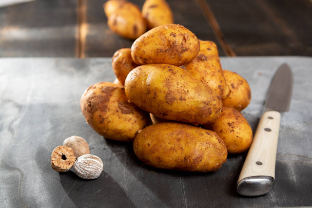 Pommes de terre de nouvelle récolte non lavées avec de la terre sur la table avec noix de muscade
 - Photo, image